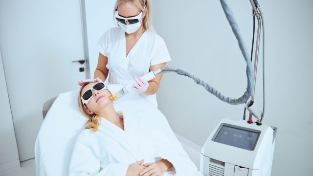 Blonde Caucasian dermatologist doing the laser resurfacing Focused doctor in safety goggles carrying out the skin tightening procedure on a female patient